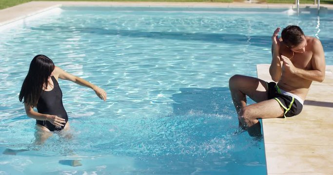 Girlfriend splashing her flinching boyfriend with cold water at outdoor swimming pool