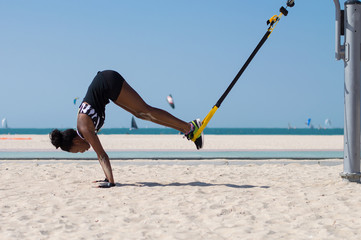 Young african woman performing difficult exercise using ropes for suspension training at Dubai beach in UAE - obrazy, fototapety, plakaty