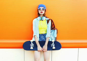 Fashion pretty cool girl with skateboard over colorful orange ba