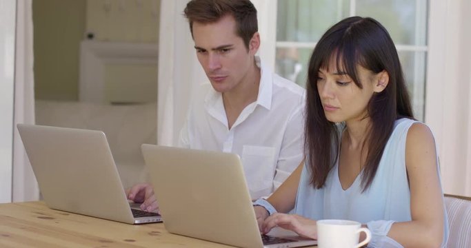 Man and woman at wooden table working on laptop computers together as they collaborate on a project online