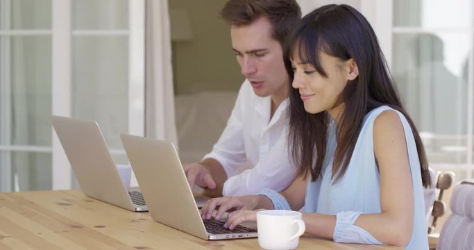 Attractive young man and woman at wooden table working on laptop computers together as they collaborate on a project or browse the internet wirelessly