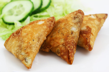 Three Indian samosas with green lettuce and slices of cucumber on the side, closeup
