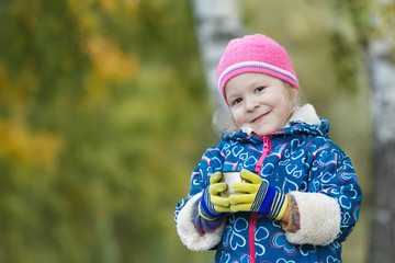 Fall outdoor head and shoulders portrait of little girl holding steel thermos flask cup in hands