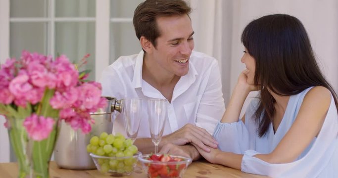 Cute mixed couple enjoying wine and fruit snacks together at table with pink flower bouquet