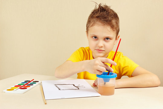Little artist in a yellow shirt painting with watercolors