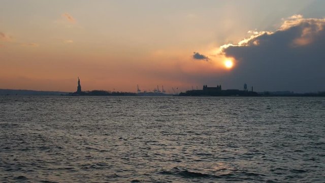 Clip of the Statue of Liberty at sunset with boat passing in front.