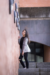 Chica joven morena subiendo y bajando feliz las escaleras en la ciudad. Modelo morena posando en las escaleras.