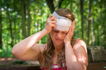 Woman applying bandage on her head after injury in nature