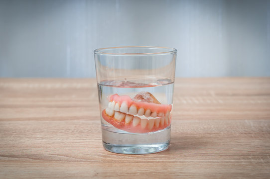 False teeth swim in transparent water glass