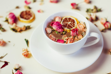 Fototapeta na wymiar Herbal tea in white Cup and saucer with roses and dried flowers dried round slices of lemon laid on a white background