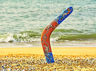 Colorful boomerang on sandy beach against sea surf. - obrazy, fototapety, plakaty