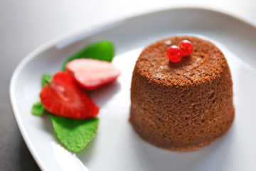 Tasty chocolate fondant with red currant and strawberry on white plate, closeup