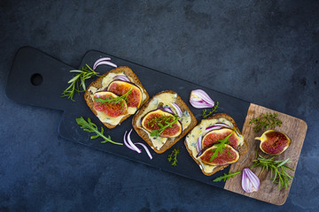 Baked toasted of dark bread with blue cheese and figs served on cutting board.