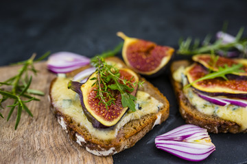 Baked toasted of dark bread with blue cheese and figs served on cutting board.