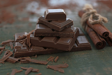 Pile of milk chocolate bars and cinnamon on old wooden background