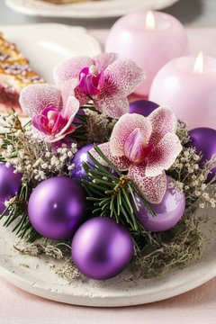 Woman making christmas decorations with violet balls, fir and or