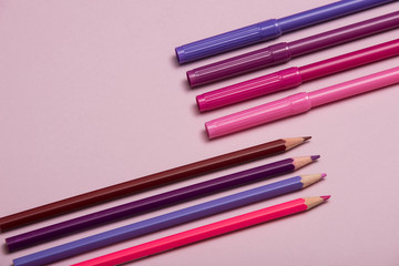 Colourful pencils, thumbtacks and clips over a pink background