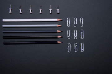 Colourful pencils, thumbtacks and clips over a black background