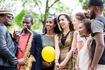 Straßenkünstler spielt Saxophon für eine multiethnische Party Gruppe junger Frauen auf...