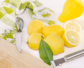 Lemons, squeezer, Zester, knife and wooden cutting board.