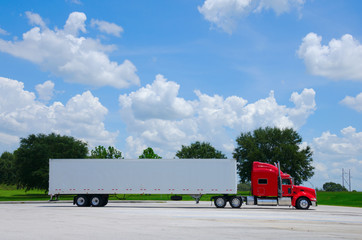 Clean shiny red 16-wheel semi tractor truck with a clean white cargo container trailer against a simple colorful background of trees and blue sky - 118763879