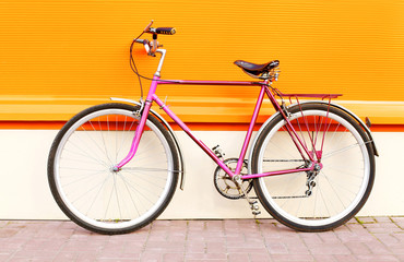 Retro pink bicycle stands over colorful orange background