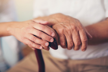 Young woman holding hand of old man with walking stick