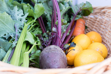 Close up of freshly picked homegrown greens, beetroot, lemons and carrots in wicker basket reading for juicing or cooking (selective focus)