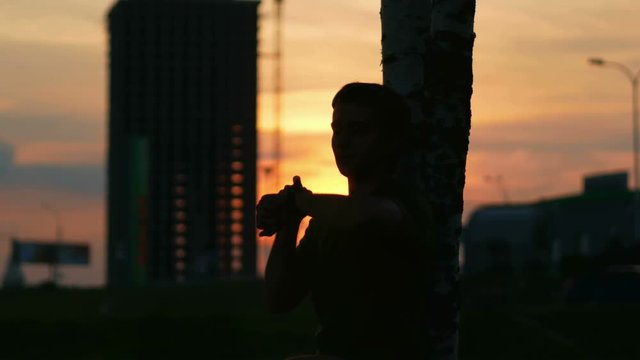Athlete man resting at sunset and check the pulse for a smart watch. City landscape with cars and construction site