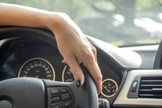 The hand of a girl with a stylish manicure turns the wheel in the car