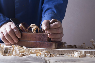 Carpenter working with plane on wooden background at Building Site. Joiner workplace