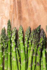 bunch of fresh asparagus stems on brown wooden cutting board with copy space, vertical, close up