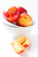sweet, organic red and yellow plums in a white bowl with some slices, isolated on white table, close up, vertical