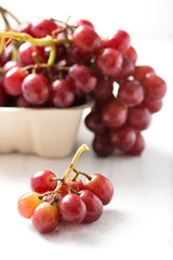 bunch of ripe, organic, seedless purple grapes in recyclable box with a small cluster in selective focus, isolated over white board, close up, vertical
