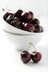 brightly lit, fresh, organic cherries in white bowl, couple of cherries in selective focus at front, isolated on white wooden background, vertical