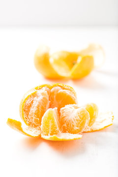 fresh and juicy mandarin orange, peeled on white background with selective focus on slices, close up, vertical