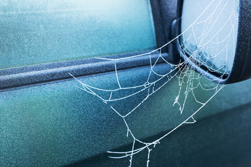 frozen spider web covered with frost early in the morning on side view mirror of a car, winter time, cold blue colors, horizontal