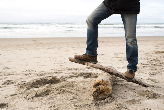 young adult man balancing on a dead log on beach