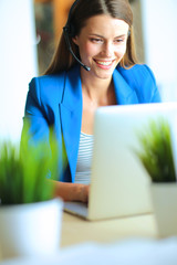 Portrait of beautiful business woman working at her desk with headset and laptop.