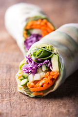 close up of fresh and vegan rice paper spring rolls with raw vegetables (cucumber, avocado, lettuce, carrots, red cabbage) inside, isolated over dark, wooden background