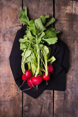 bundle of organically grown, freshly harvested, red radishes, isolated over black kitchen cloth and rustic wooden background, close up, top view