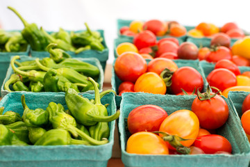 fresh cherry tomatoes and green peppers in disposable boxes side by side, on display in a farmers market, horizontal