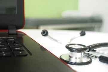 Black stethoscope next to a laptop with examination table in the background