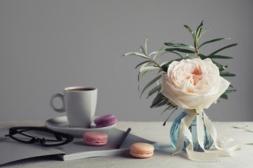 Morning still life with vintage rose in a vase, coffee and macarons on a light table. Beautiful and cozy breakfast.