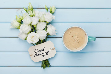 Coffee mug with white flowers and notes good morning on blue rustic table from above. Beautiful...