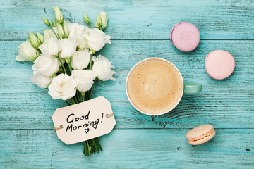 Coffee mug with macaron, white flowers and notes good morning on blue rustic table from above....