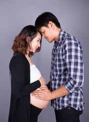 young couple: pregnant mother and happy father on gray backgroun
