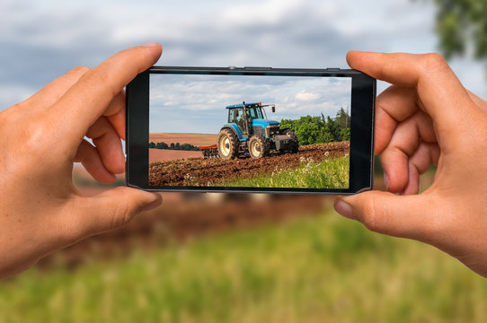 Taking photo of tractor at work on a field with mobile phone