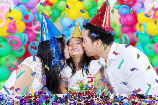 Girl kissed by her parents at birthday party