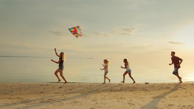 Group of children playing with adults. Let them into the sky kite fun running on the beach